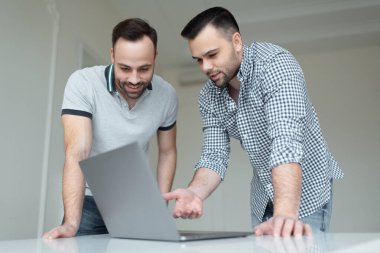 Bilgisayarda çalışan kendine güvenen iki iş adamının portresi. Bir adam akıllı telefondan konuşuyor, diğeri ekranı işaret ediyor..