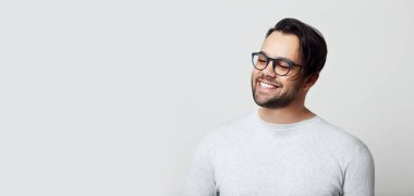 Beyaz arka planda beyaz dişli, gözlüklü, gülümseyen genç bir adamın portresi..