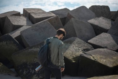 Sırt çantalı genç bir adam portresi, yeniden kullanılabilir çelik termo su şişesi kullanıyor, arka planda kare taşların üzerinde..