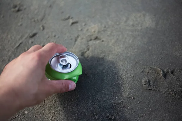 Close-up of male hand holding a can of soda on the beach.