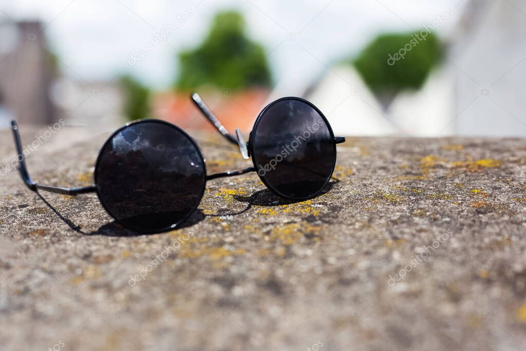 Close-up of black round sunglasses on stone.