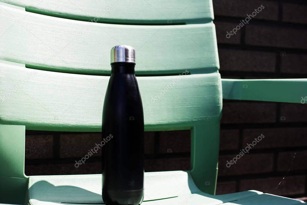 Close-up of reusable thermo water bottle on green chair.