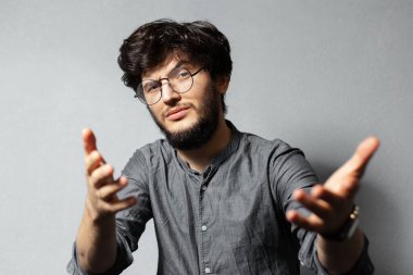 Dağınık saçlı ve gözlüklü, kendine güvenen sakallı adamın portresi gri arka plandaki kamerayı işaret ediyor..