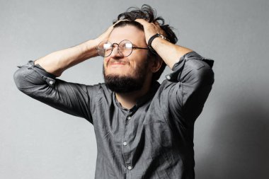 Dağınık saçlı ve gözlüklü genç sakallı adamın portresi, el ele tutuşun. Gri desenli arka plan.