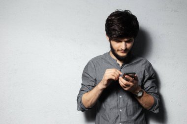 Akıllı telefon kullanan kendine güvenen bir gencin portresi. Sakallı hippi. Gri rengin desenli arka planı.