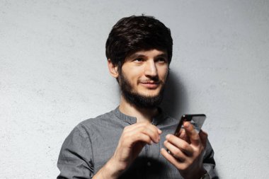 Akıllı telefon kullanan kendine güvenen bir gencin portresi. Sakallı hippi. Gri rengin desenli arka planı.