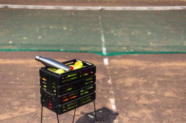 İçinde bir sürü tenis topu ve su için bir adet çelik termo şişe olan kara kutu. Tenis kortunda. Plastik şişelere hayır de..