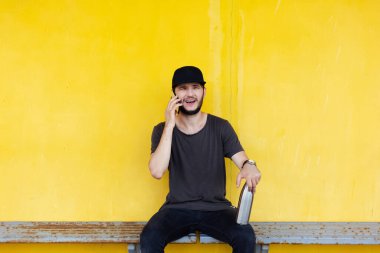 İstasyon sandalyesinde oturan genç adam, akıllı telefonla konuşuyor, bacağındaki su için çelik termometreyi tutuyor. Sarı arkaplan.