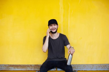 Gülümseyen adam sarı arka planda, çelik termo şişenin yanında oturuyor ve akıllı telefondan konuşuyor..