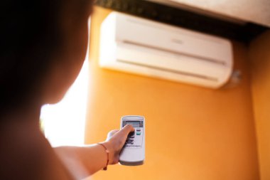Çocuk elinin turuncu arka planda uzaktan kumandalı klimayı ayarlaması.