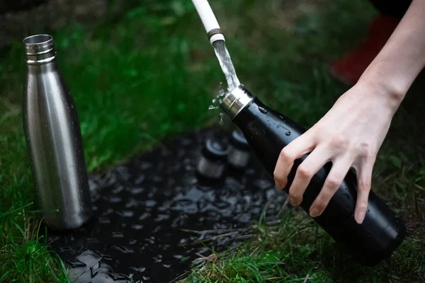 Kadın eli paslanmaz termo şişeyi tutar ve suyla doldurur..