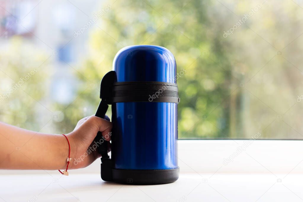 Close-up of hand hold blue thermos.
