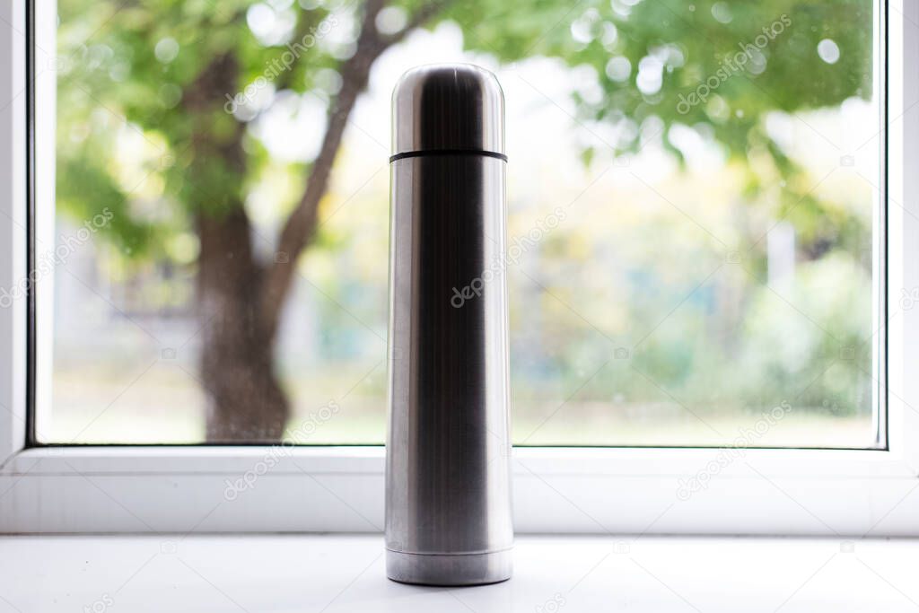 Steel thermos on window background.