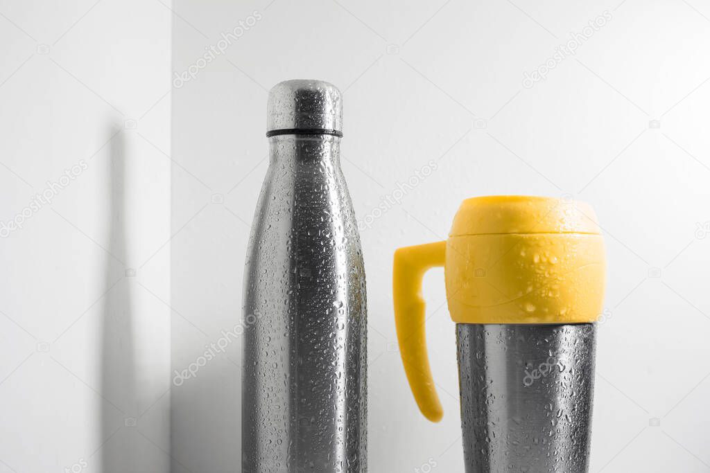 Yellow steel thermo mug and eco stainless thermal bottle sprayed with water on white background.
