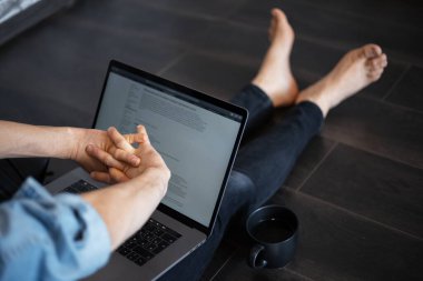 Dizüstü bilgisayarda çalışan bir adam yerde oturuyor..