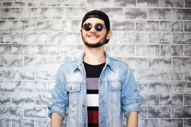 Gri tuğla duvarın arka planında mavi kot ceketli genç adamın portresi..