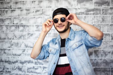 Gri tuğla duvarın arka planında mavi kot ceketli genç adamın portresi..