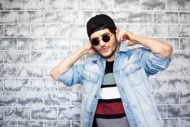 Gri tuğla duvarın arka planında mavi kot ceketli genç adamın portresi..