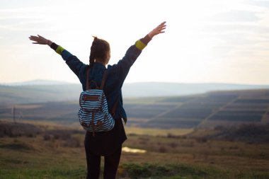 Sırt çantalı, kot ceketli genç bir kızın arka plan portresi günbatımında ve tarlalarda..