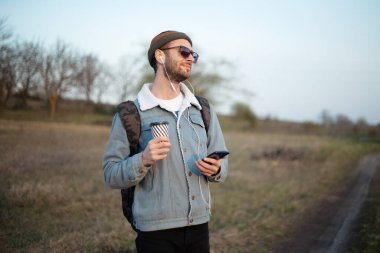Elinde bir fincan sıcak kahve ve kulaklıklı akıllı telefon tutan genç adamın portresi..