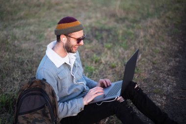 Dışarıda dizüstü bilgisayar kullanan genç hippi portresi..