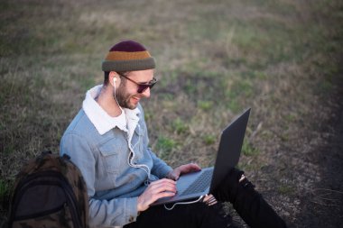 Dışarıda dizüstü bilgisayar kullanan genç hippi portresi..