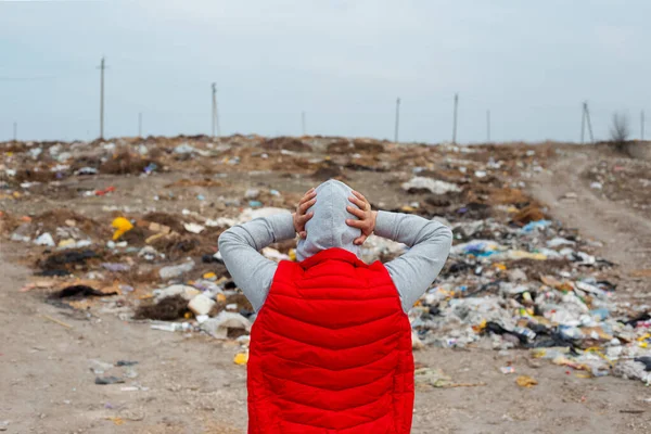Back view of human with hands on head looking on a lot of garbage.