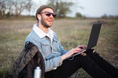Dışarıda dizüstü bilgisayar kullanan genç hippi portresi..