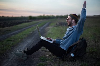 Millennial hipster dizüstü bilgisayarda çalışan kulaklıklı adam gün batımında sahada..