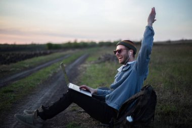 Millennial hipster dizüstü bilgisayarda çalışan kulaklıklı adam gün batımında sahada..