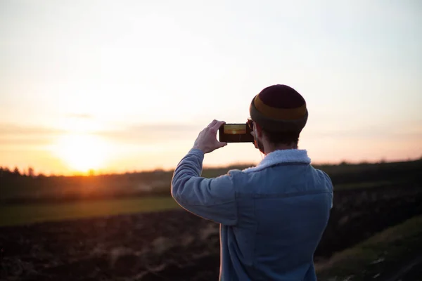 Günbatımını Akıllı Telefondan Çeken Genç Adamın Arka Plan Görüntüsü — Stok fotoğraf
