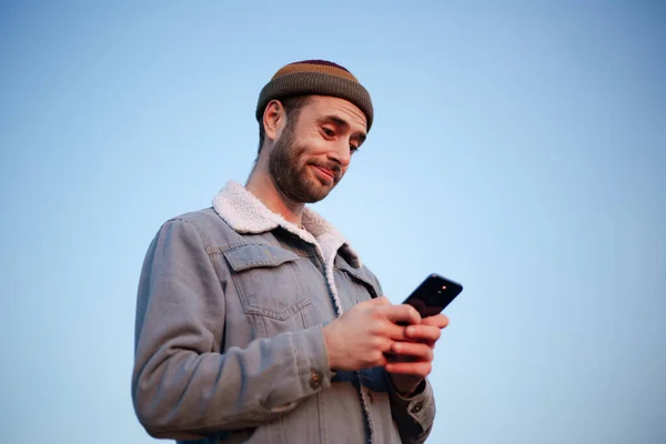 Portret Uśmiechniętego Nowoczesnego Faceta Smartfonem Rękach Tle Błękitnego Nieba — Zdjęcie stockowe