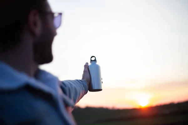 夕日を背景に水用アルミボトルを持っている男の手 — ストック写真