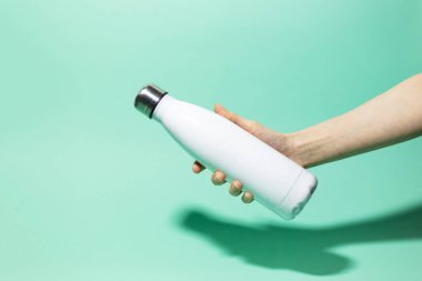Kadın elinin, arka planda bulunan beyaz, yeniden kullanılabilir çelik, paslanmaz termodinamik su şişesini tutuşu. Plastiksiz.