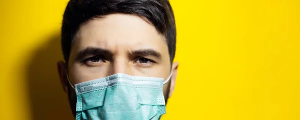 Close-up portrait of male face, wearing medical flu mask on background of yellow color with copy space.