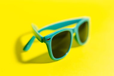 Cyan güneş gözlüklerinin yakın plan görüntüsü, sarı arkaplan.
