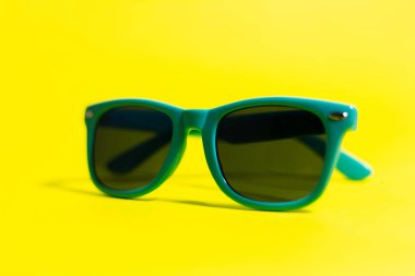 Cyan güneş gözlüklerinin yakın plan görüntüsü, sarı arkaplan.