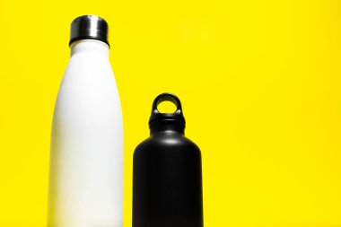 Yarı yeniden kullanılabilir iki eko, çelik ve alüminyum, termo su şişesi, beyaz ve siyah renkli, sarı arka planda izole edilmiş..