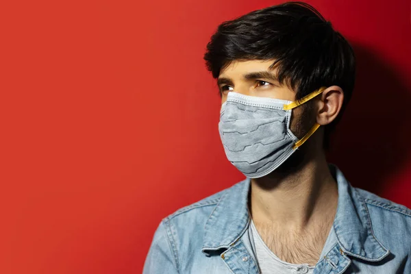 Tıbbi grip maskesi takan genç bir adamın stüdyo portresi, arka planda kırmızı renk ve fotokopi alanı..