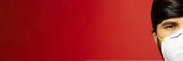 Coronavirus 'a karşı beyaz tıbbi grip maskesi takmış yarı erkek yüzünün yakın plan portresi. Kopya alanı ile kırmızı panoramik arkaplanda izole.