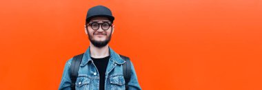 Banner panoramik portresi kot ceket, kep, sırt çantası ve gözlük giyen güler yüzlü hippi adam arka planda bulunan yemyeşil lav rengi fotokopi alanı ile izole edilmiş..