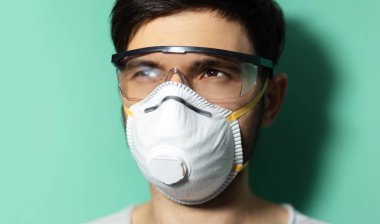 Tıbbi maske takan ve koronavirüse karşı koruyucu gözlük takan genç adamın yakın plan stüdyo portresi..
