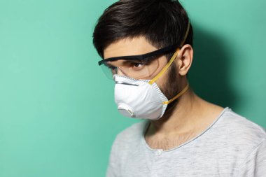 Stüdyo profil portresi tıbbi grip maskesi ve gözlük takan genç adam, koronavirüse karşı korunma, arka planda su menileri rengi.