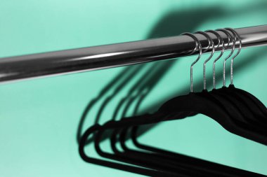 Aqua menthe renginin arka planında siyah boş askıları olan elbise askılarının yakın plan görüntüsü.