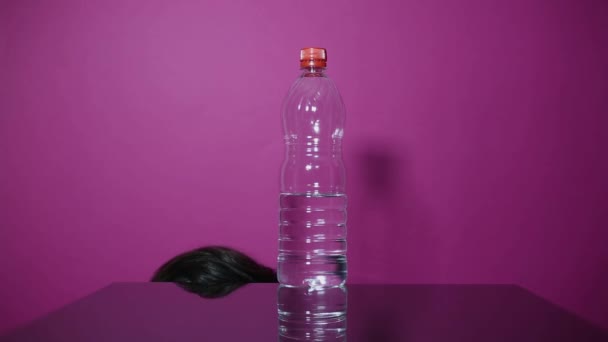 若い男はプラスチックボトルをガラステーブルの上のスチール熱水ボトルに変え ピンク色の背景 — ストック動画