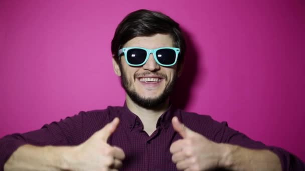 年轻快乐的家伙戴着粉色背景的青色太阳镜竖起大拇指的画像 — 图库视频影像