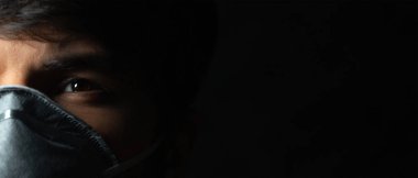 Coronavirus önleme. Siyah arka planda gribe karşı koruyucu solunum maskesi takan genç adamın yakın plan portresi. Makro fotoğraf.