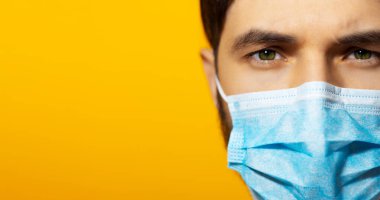 Coronavirus 'a karşı tıbbi solunum maskesi takan genç bir adam. Sarı arkaplanda kopya alanı ile panoramik portre.
