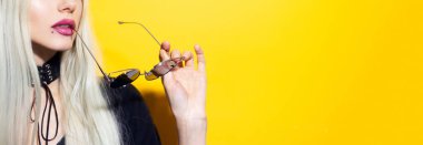 Yakın çekim stüdyo resmi, sarı arka planda güneş gözlüğü tutan genç sarışın kız fotokopi alanı ile..