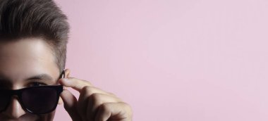 Stüdyonun yarı yüz portresi açık pembe rengin arka planına güneş gözlüğü taktı..